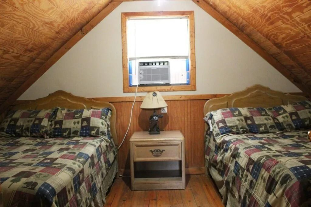 Small attic bedroom with two twin beds, wood paneling, and a window air conditioner.