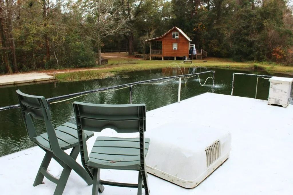 Snow-covered dock chairs beside a pond, with a small red cabin across the water.