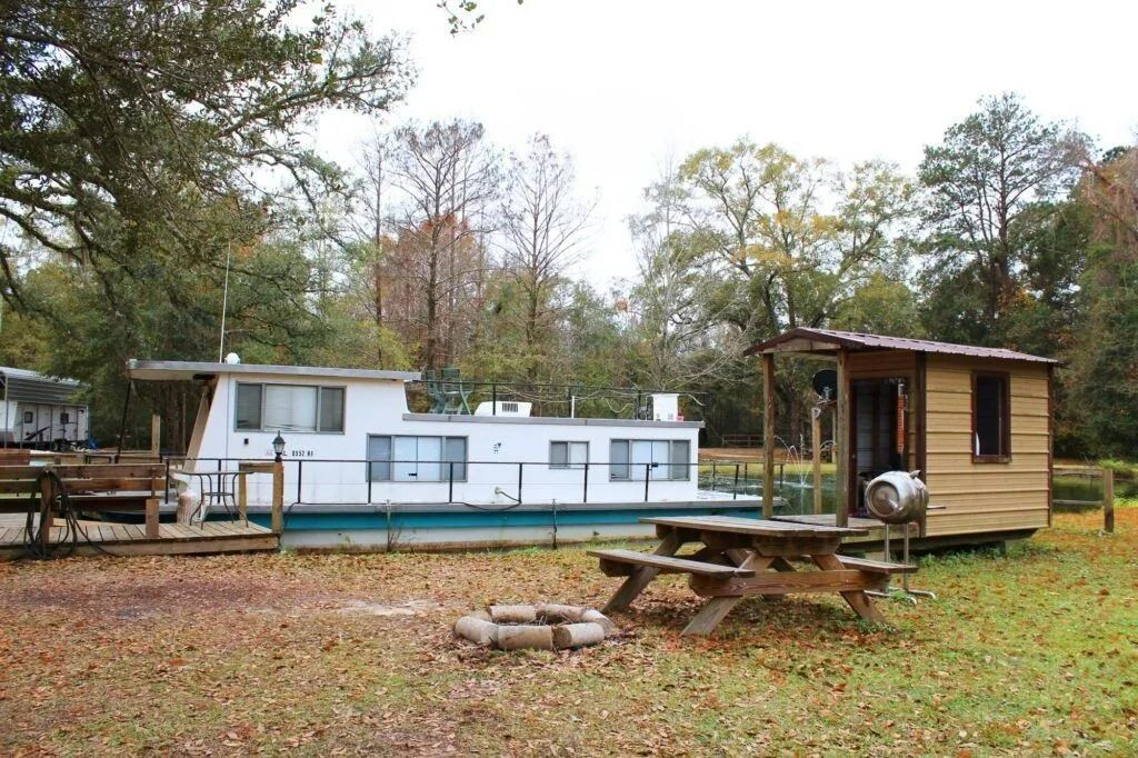 Rural campsite with a white trailer, wooden cabin, picnic table, and autumn trees