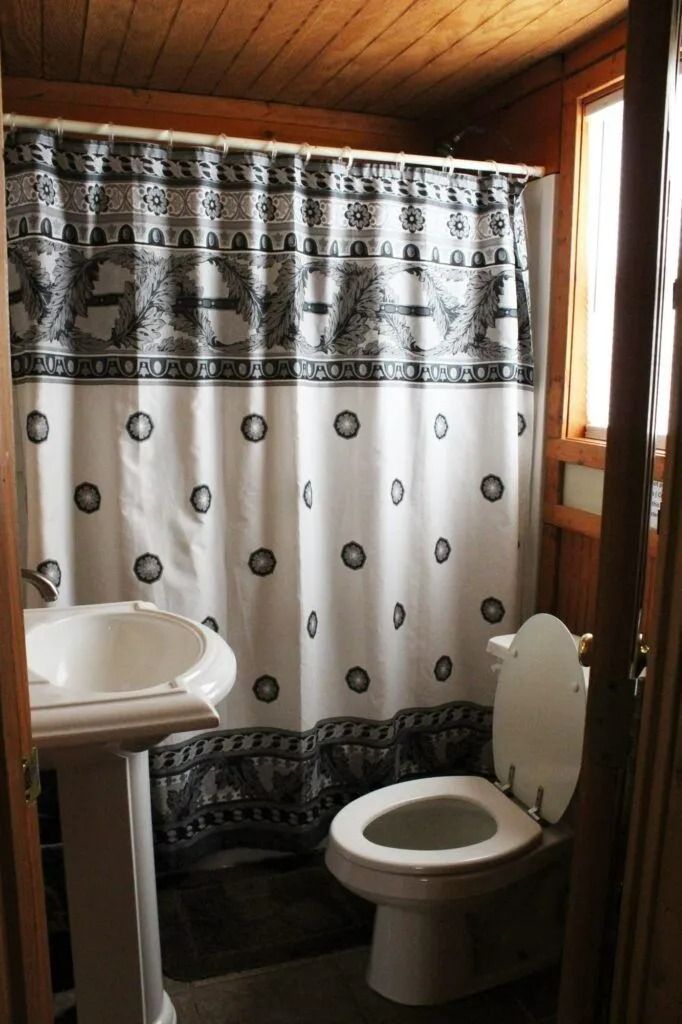 Small bathroom with white toilet, sink, and black-and-white shower curtain in a wooden cabin.