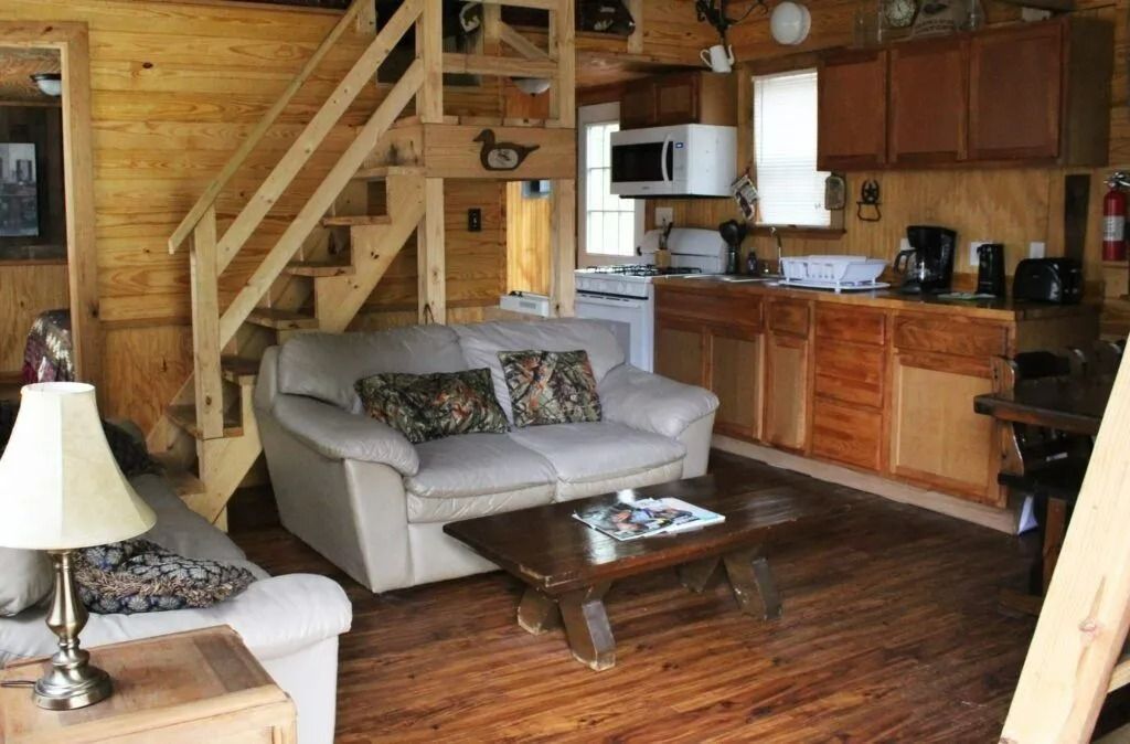 Cozy cabin living room with wood stairs, sofa, coffee table, and kitchenette