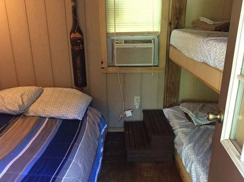 Small cabin bedroom with bunk beds, striped bedding, and a window air conditioner.
