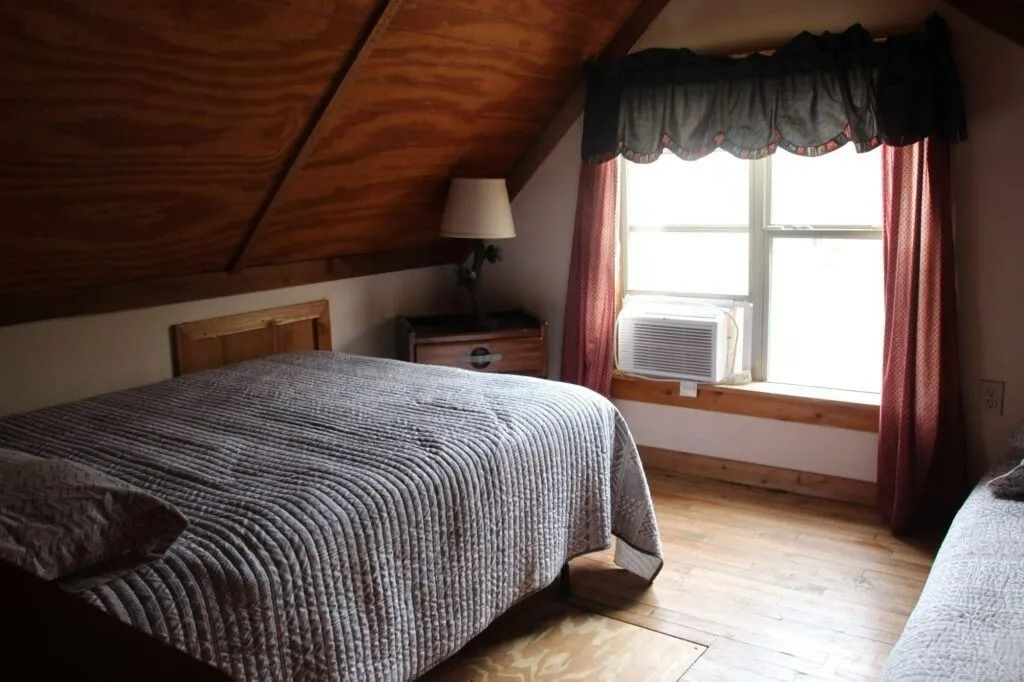 Cozy bedroom with sloped wood ceiling, bed, lamp, and window with dark curtains