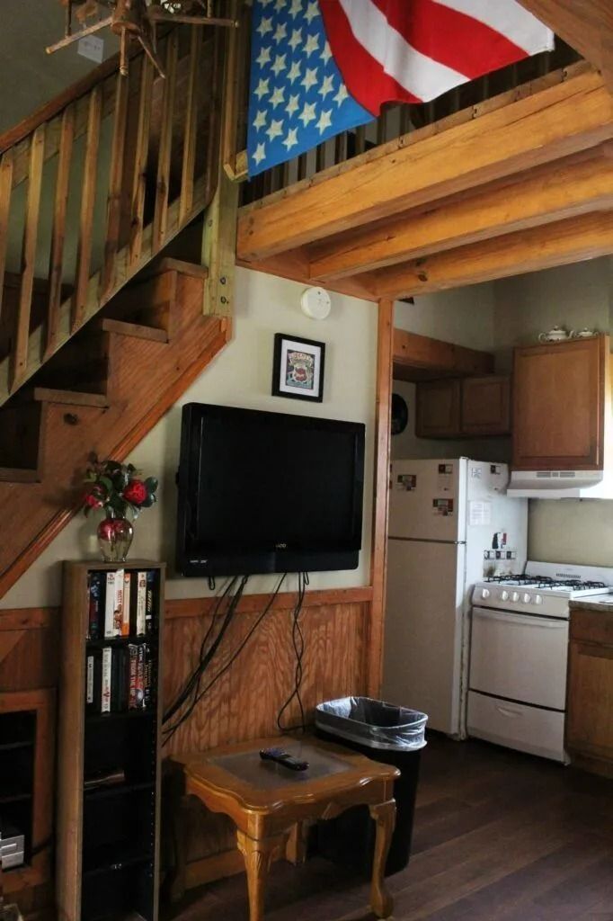 Small loft kitchen and living area with staircase, TV, wooden furniture, and U.S. flag decor.