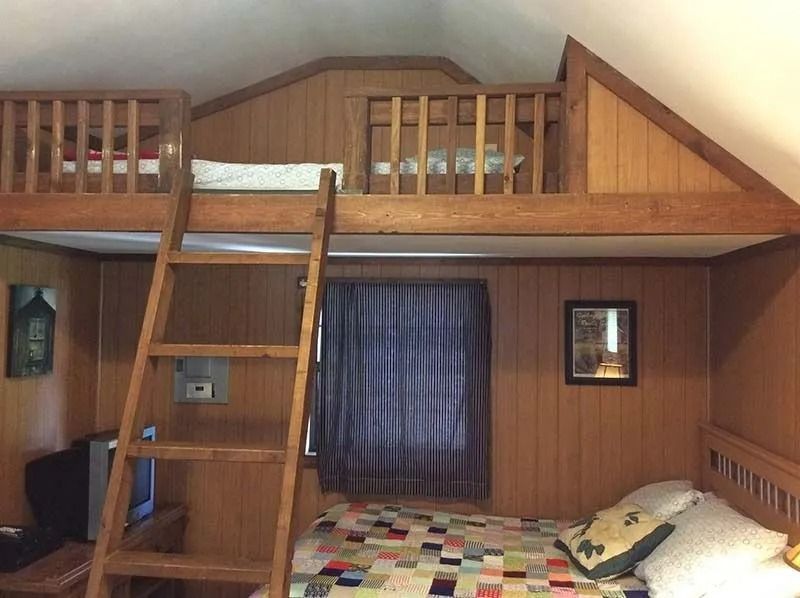 Loft bedroom with wooden bunk beds, a ladder, and a window with dark curtains