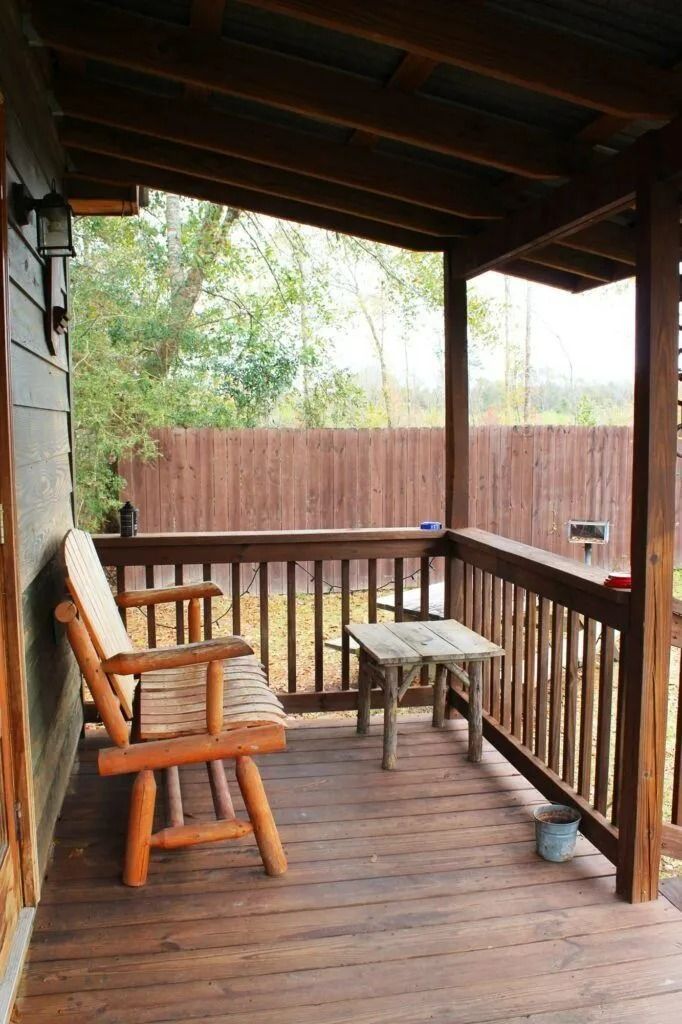 Wooden porch with a rocking chair, small table, and railing overlooking trees and a fence