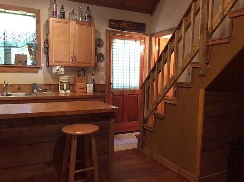 Warm kitchen with wooden cabinets, island stool, back door, and staircase along the right wall.
