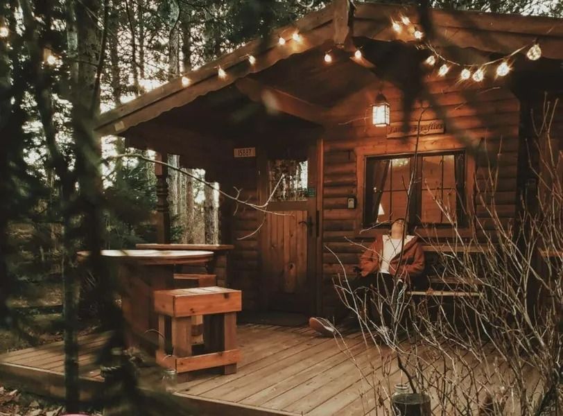Cozy wooden cabin porch with string lights and a person relaxing in a chair at dusk