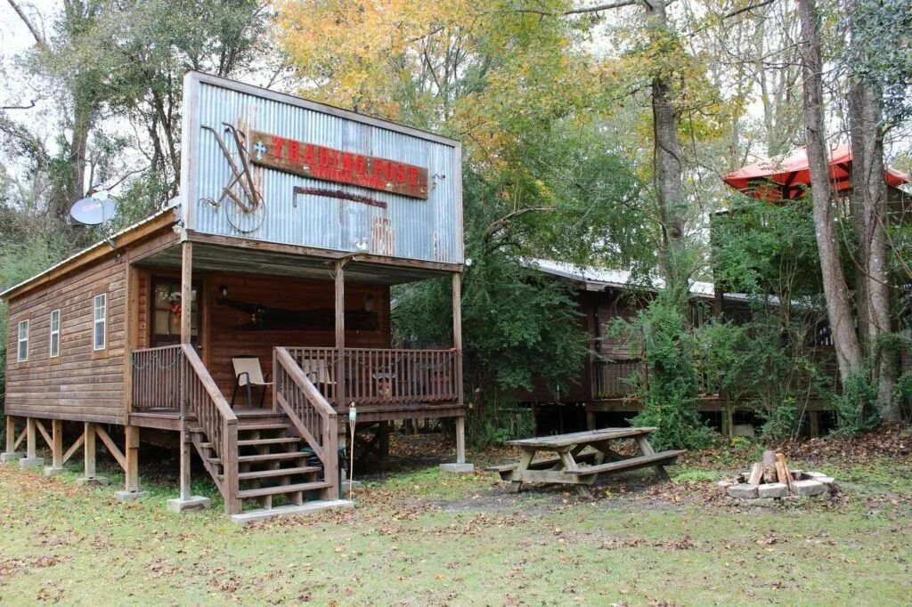Rustic wooden cabin with porch and sign, surrounded by trees and grass.