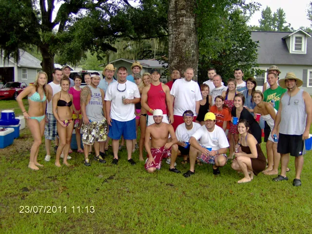 Group of people posing together outdoors on a grassy lawn in front of a house.