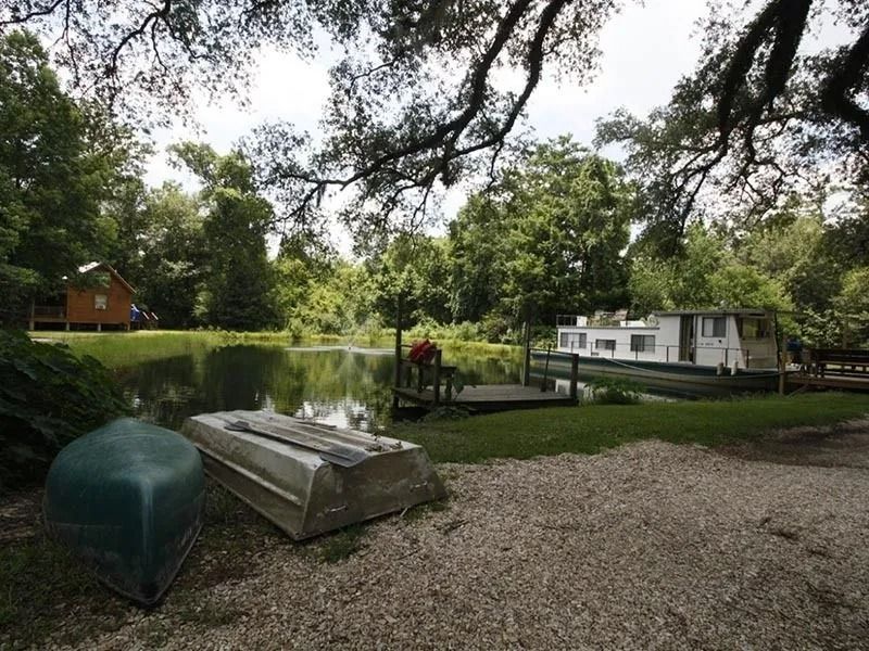 Lakeside campsite with canoes, a dock, and trees under a cloudy sky.