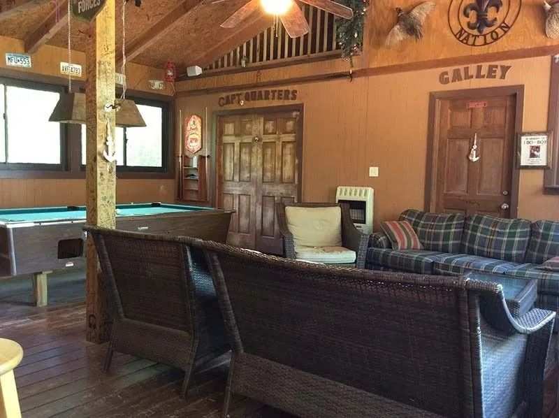 Cozy rustic lodge lounge with wood beams, pool table, plaid couch, and wicker seating