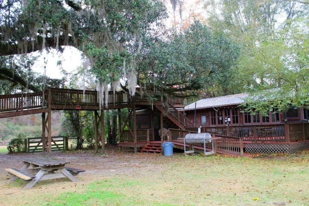 Wooded outdoor picnic area with raised wooden deck, tables, and a rustic cabin-like shelter