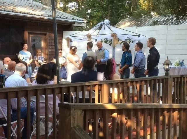 People gathered outdoors in a courtyard, standing by a wooden railing near a white canopy.