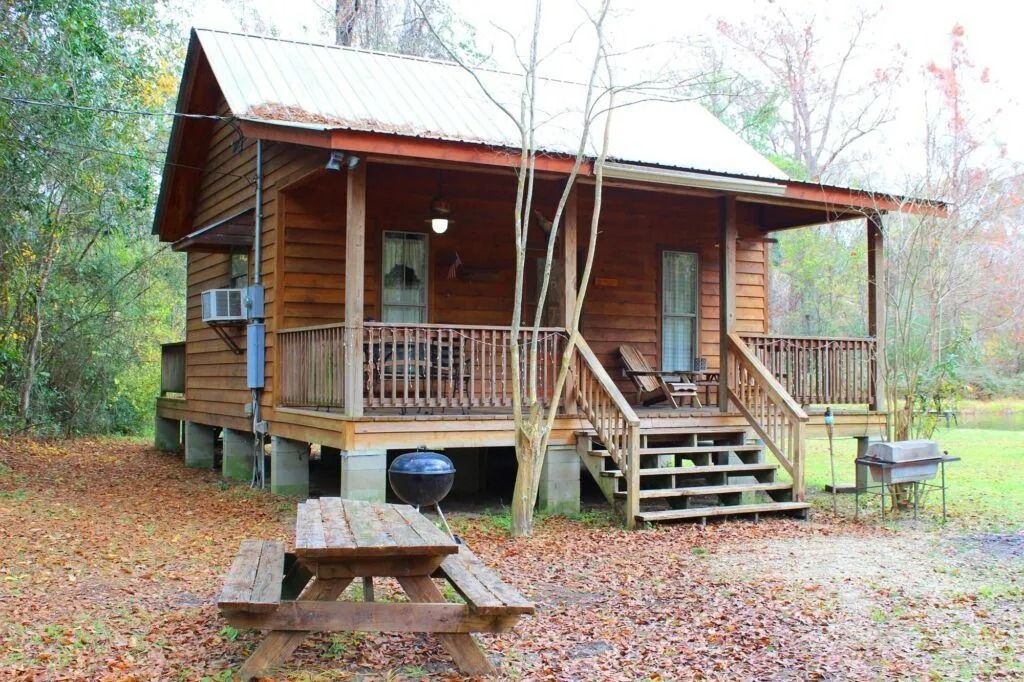 Wooden cabin in a leaf-covered yard with a front porch, steps, and picnic table in a wooded setting