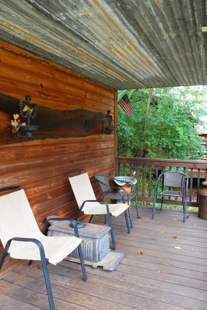 Covered wooden porch with chairs and a small table beside a lush green yard