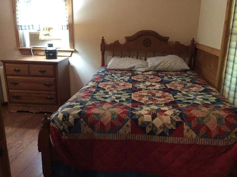 Bedroom with wooden bed, colorful quilt, dresser, and bright window on the left.