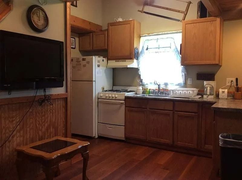 Small kitchen with wooden cabinets, white stove and refrigerator, and a bright window over the sink.