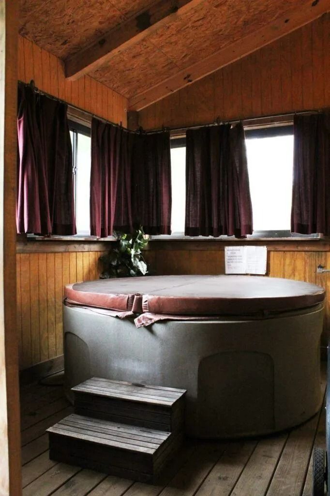 Round hot tub in a wood-paneled room with curtained windows and steps leading up to it