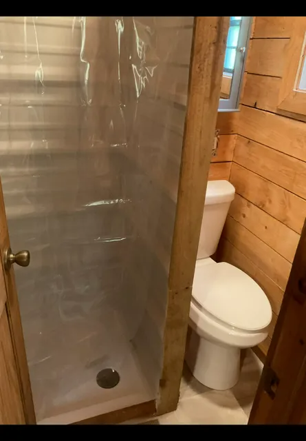 Small bathroom with wooden walls, shower stall on the left, and white toilet beside it.