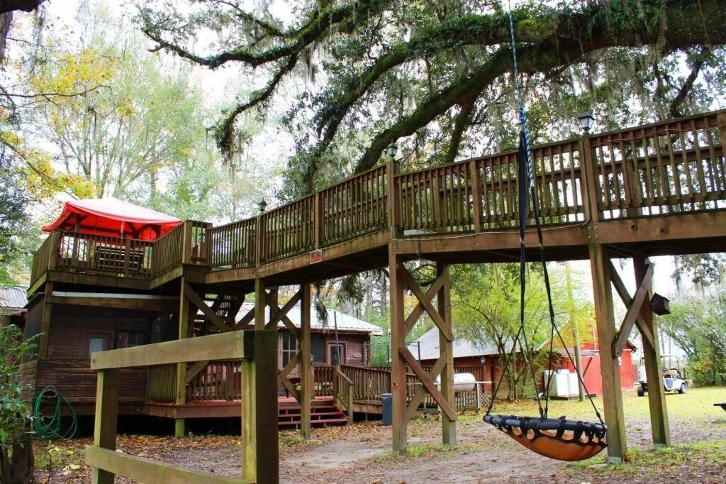 Wooden elevated playground with bridges, slides, and swings under trees in a park