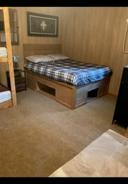 Small wood-paneled bedroom with a single bed, plaid bedding, and a beige carpet.
