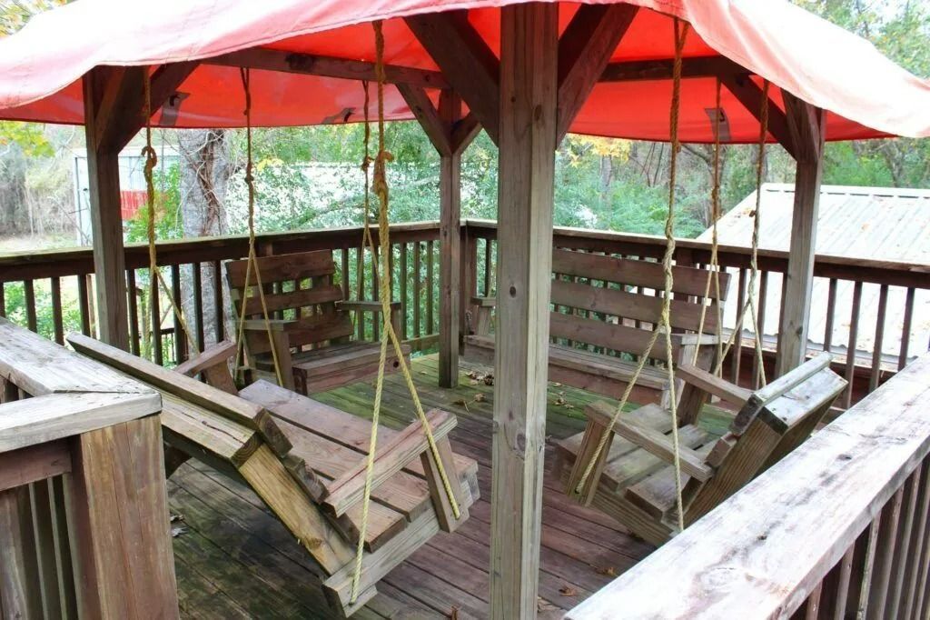 Rustic wooden gazebo with a red canopy and hanging swings in a wooded outdoor setting
