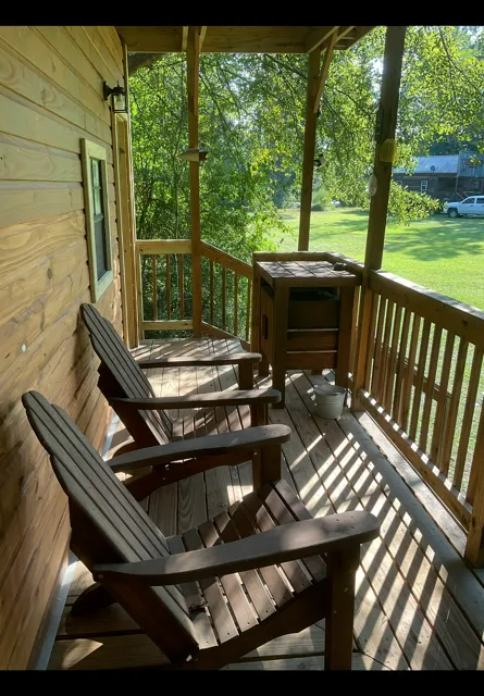 Wooden porch with two chairs, a small table, and a green yard beyond the railing.