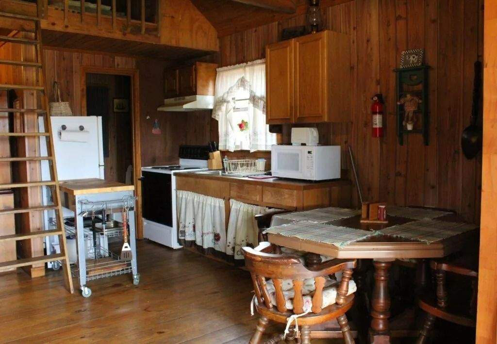 Rustic wooden kitchen with table, chairs, white appliances, and a ladder by the fridge