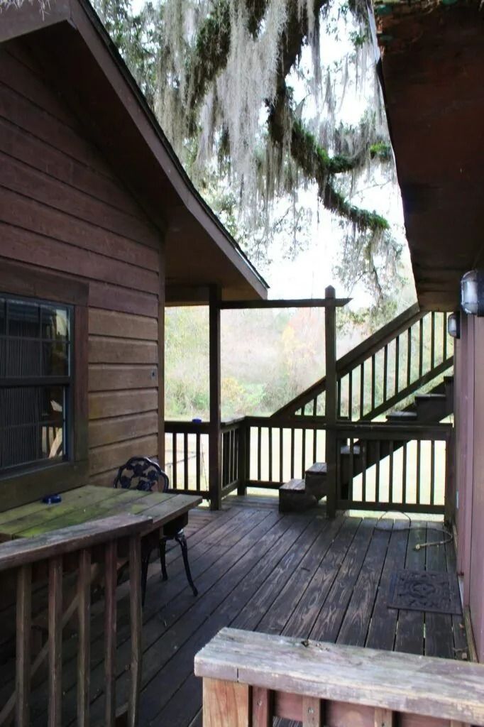 Wooden cabin deck with stairs, railing, and a table overlooking a misty forest.