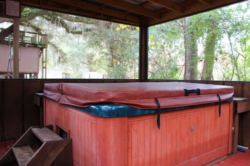Covered red hot tub on a wooden deck under a roof, with trees in the background