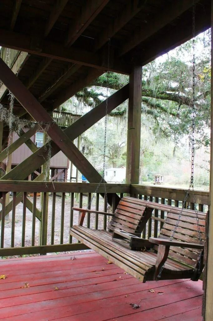 Covered wooden porch with red floorboards and a bench overlooking trees and water