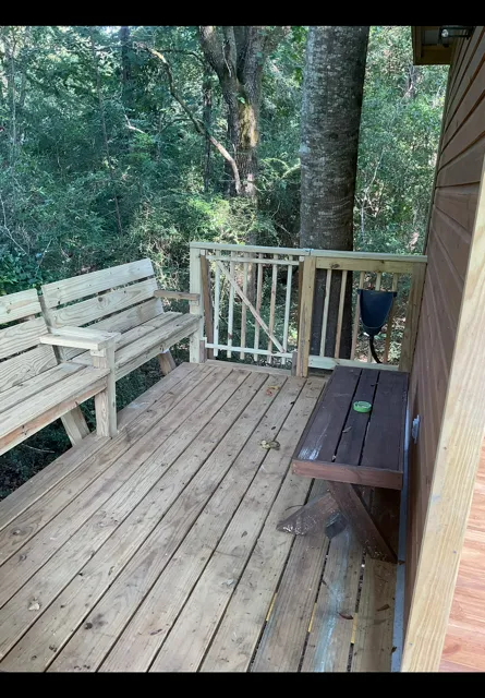 Wooden porch deck with benches, railing, and trees beyond the yard