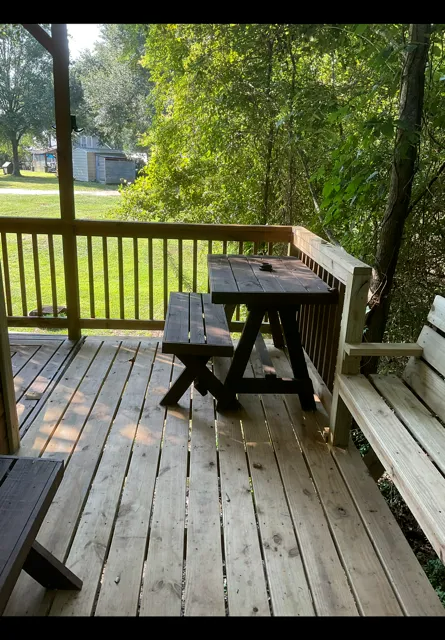 Wooden porch with picnic table and bench, overlooking a green backyard with trees and a shed.