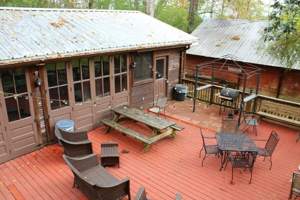 Wooden deck patio with picnic table, chairs, lounge seats, and surrounding cabin walls under a tin roof