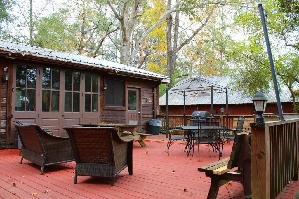 Red wooden deck with patio chairs and tables outside a rustic cabin surrounded by trees