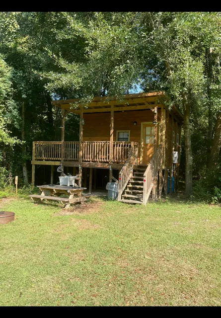 Wooden cabin porch with stairs amid trees and a grassy yard
