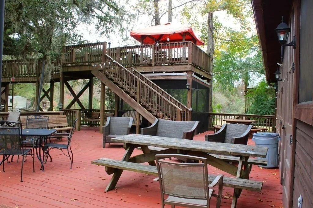 Wooden deck patio with stairs, outdoor tables, chairs, and a red umbrella under trees