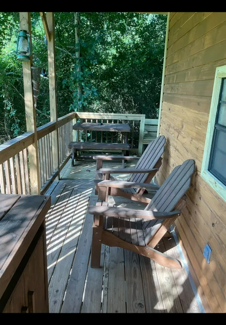 Wooden porch with two Adirondack chairs, railing, and trees beyond in dappled sunlight