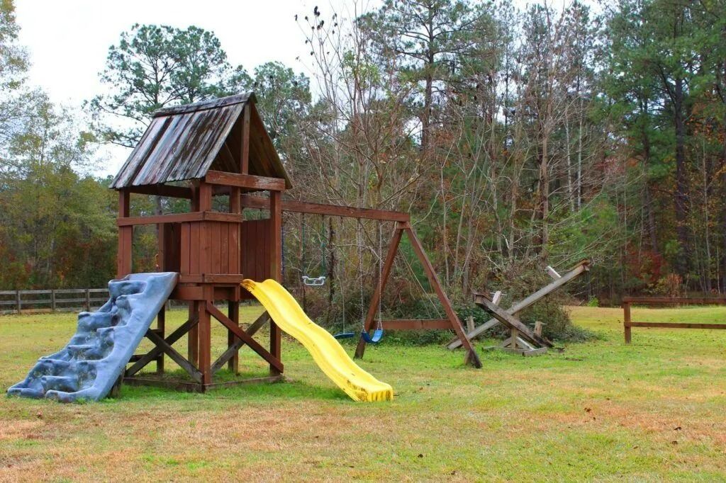 Wooden playground with blue steps, yellow slide, and a swing set in a grassy field.