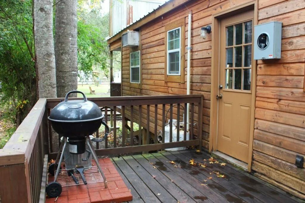 Wooden cabin deck with a black charcoal grill beside the door, surrounded by trees.