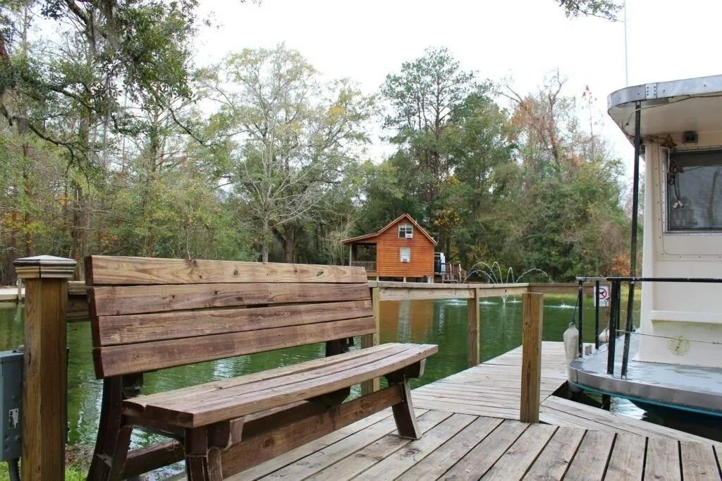 Wooden deck with bench and railing overlooking trees and a small orange cabin in the distance