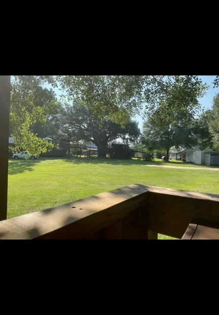 Sunny backyard with green lawn, leafy trees, and a wooden deck railing in the foreground