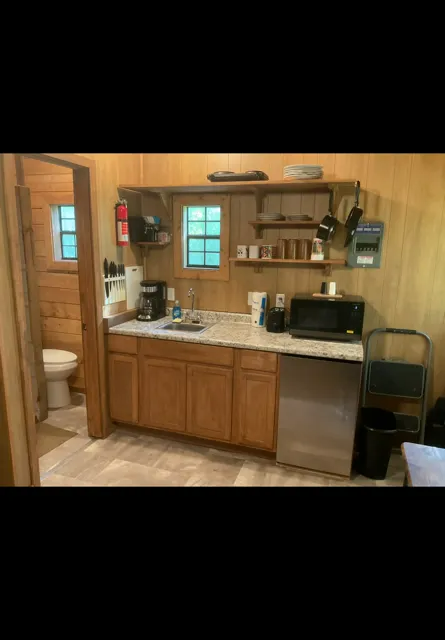 Compact wood-paneled kitchenette with sink, cabinets, stove, microwave, mini fridge, and window.