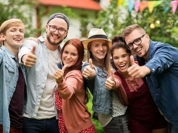 Group of friends smiling and giving thumbs up outdoors in a park