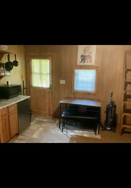Small wood-paneled kitchen with a window, table, stove, and vacuum cleaner on the right.