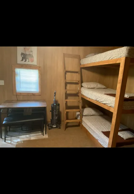 Small bedroom with bunk beds, a desk by the window, and a ladder against wood-paneled walls.