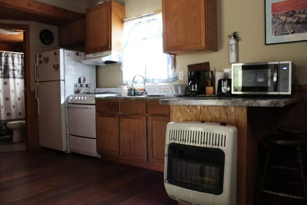 Small kitchen with wood cabinets, white appliances, granite counters, and a microwave by the stove.