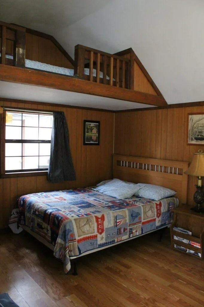 Cozy wood-paneled bedroom with a bed beneath a loft and a window on the left.