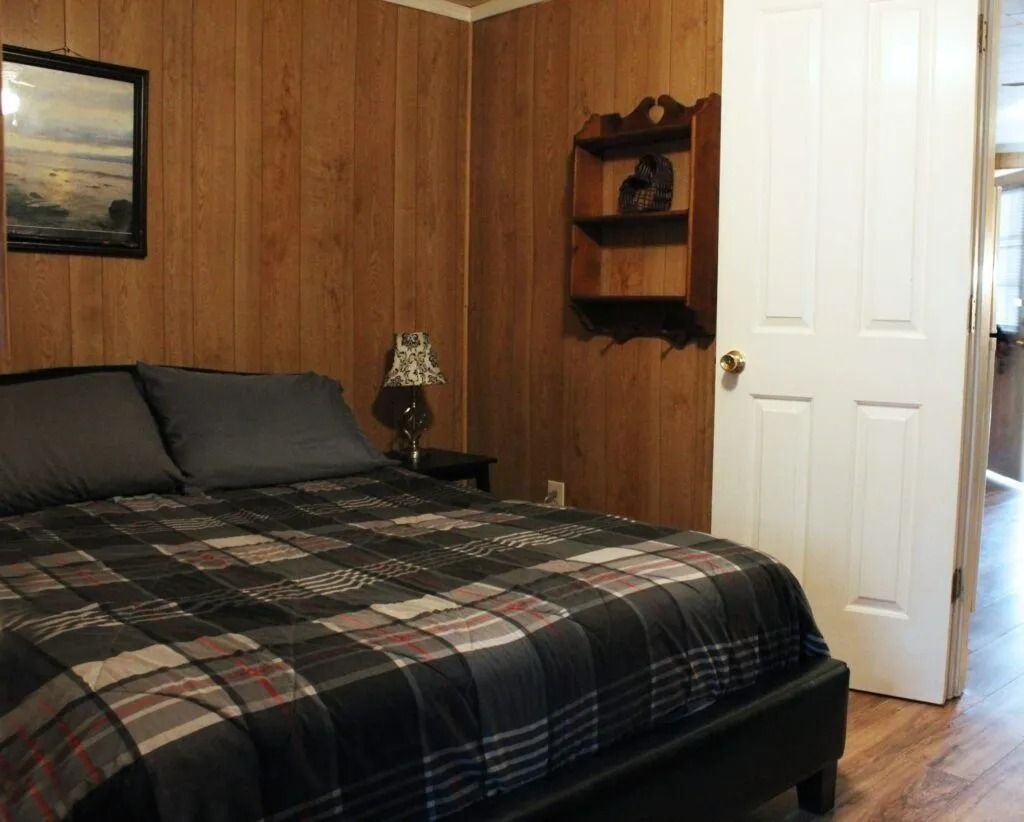 Bedroom with plaid bedspread, wood-paneled walls, white door, and corner shelves.